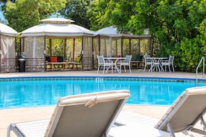 Un área de piscina con sillones, mesas y un pabellón.