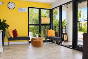 Uma área de recepção com placa de check-in/check-out, relógio, um banco, uma mesa pequena e vista para o exterior.