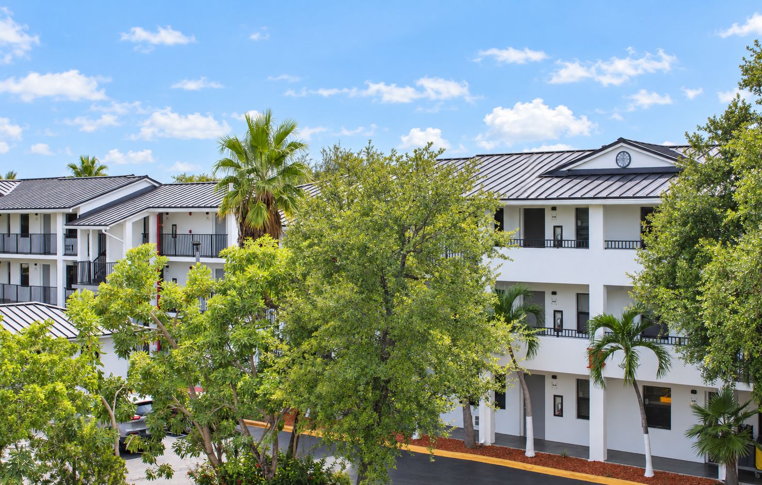 A multi-story hotel with balconies, surrounded by trees and a clear sky.