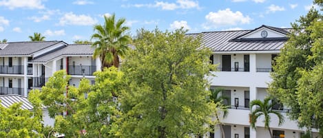 Un hotel de varios pisos con balcones, rodeado de árboles y un cielo despejado.