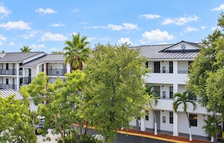 A multi-story hotel with balconies, surrounded by trees and a clear sky.