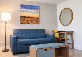 A room with a blue sofa, a small wooden table with a chair, a floor lamp, and a wall-mounted mirror.
