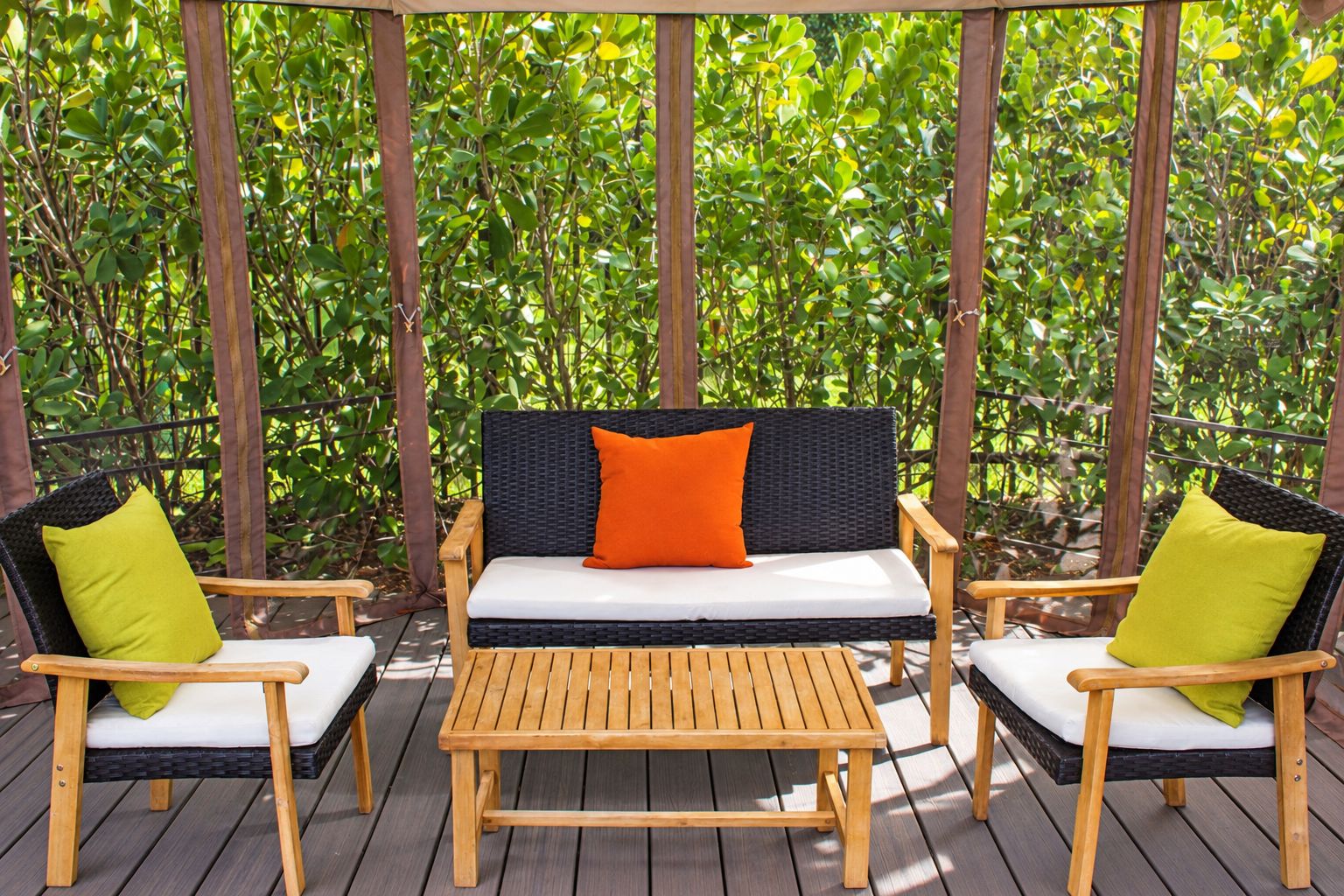 Une terrasse en bois avec un canapé en osier noir, deux chaises en bois et une table en bois.