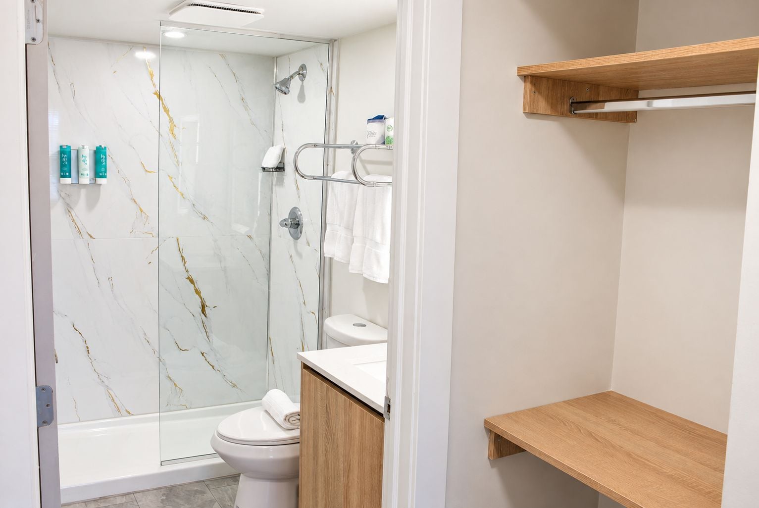 Un baño con ducha envuelta en vidrio, inodoro y estante de madera.
