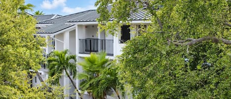 A multi-story building with balconies, surrounded by lush greenery.