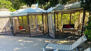 A covered outdoor seating area with lounge chairs and tables, surrounded by trees. - Nova Inn Resort (Boynton Beach)