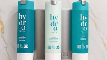Three bottles of Hydra Touch products: shower gel, conditioner, and shampoo, each with a QR code and eco-friendly symbols.