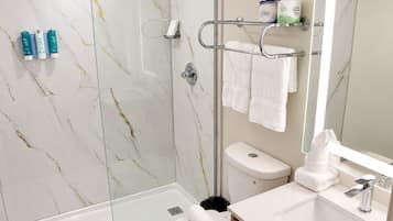 A modern bathroom with a glass shower enclosure, a toilet, a sink with a mirror, and a towel rack with multiple towels.