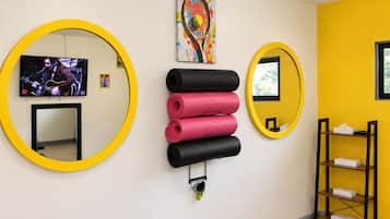 A room with two large circular mirrors, a television, a colorful abstract painting, and a shelf with yoga mats.