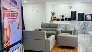 A modern living room with a sectional sofa, a flat-screen TV, a marble floor, and a clock on the wall. - Nova Inn Resort (Boynton Beach)