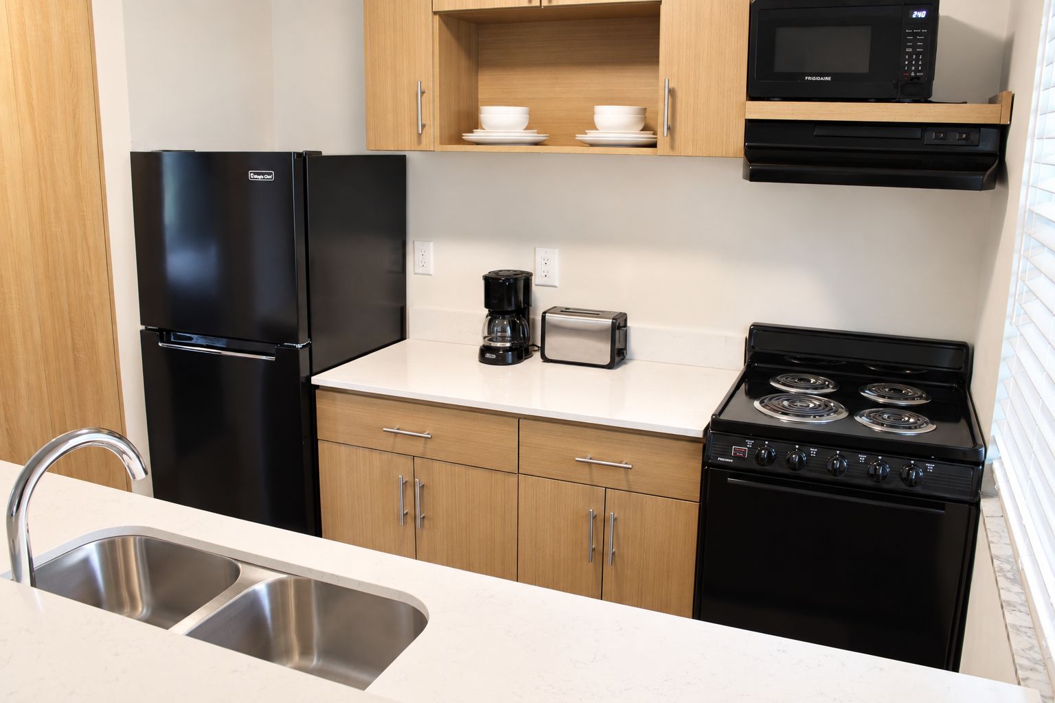 Una cocina con un refrigerador negro, estufa, microondas, tostadora y cafetera.