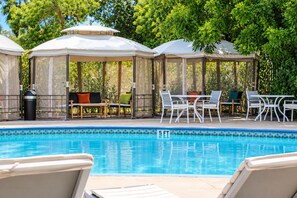 A pool area with lounge chairs, a table, and a gazebo.
