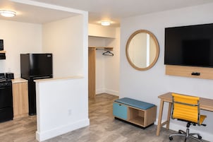 A modern kitchen with a refrigerator, stove, and a black oven. There is a wooden cabinet and a blue bench. A yellow office chair is next to a desk with a computer monitor.