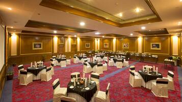 A banquet hall with round tables, white chairs, and red carpeting.