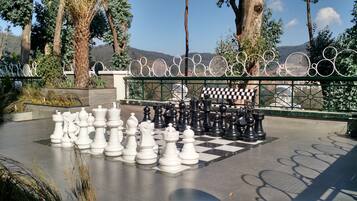 A chessboard with pieces set up outdoors, surrounded by trees and a fence.