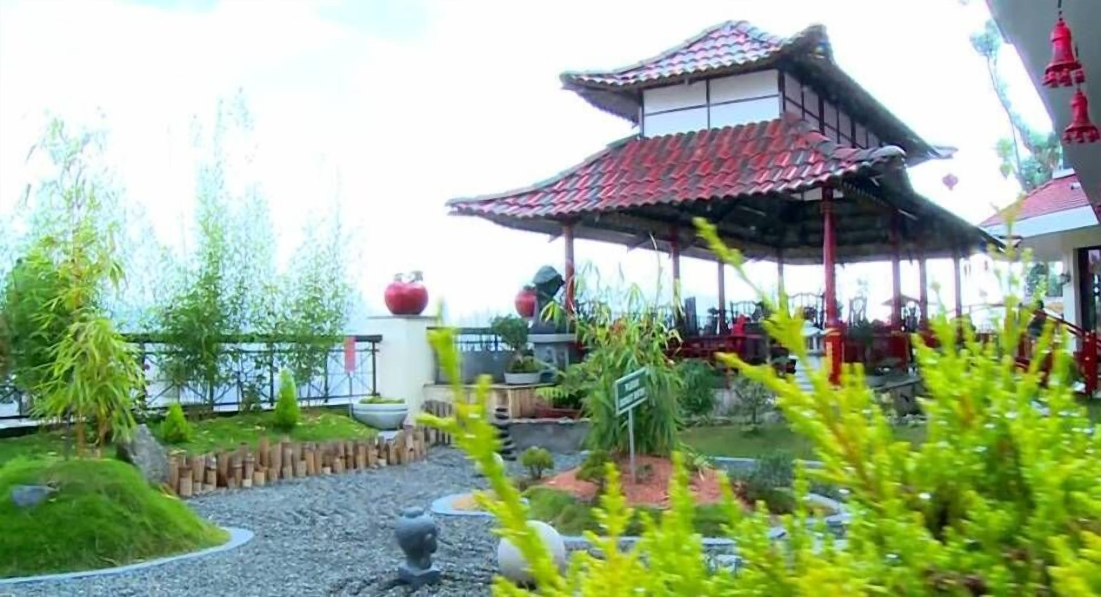 En traditionel japansk pavillon med et flisegulv, omgivet af en anlagt have med forskellige planter og en grussti.