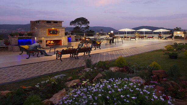 An outdoor patio area with seating, a fireplace, and a view of the hills. - Gem Park Ooty (Ootacamund)
