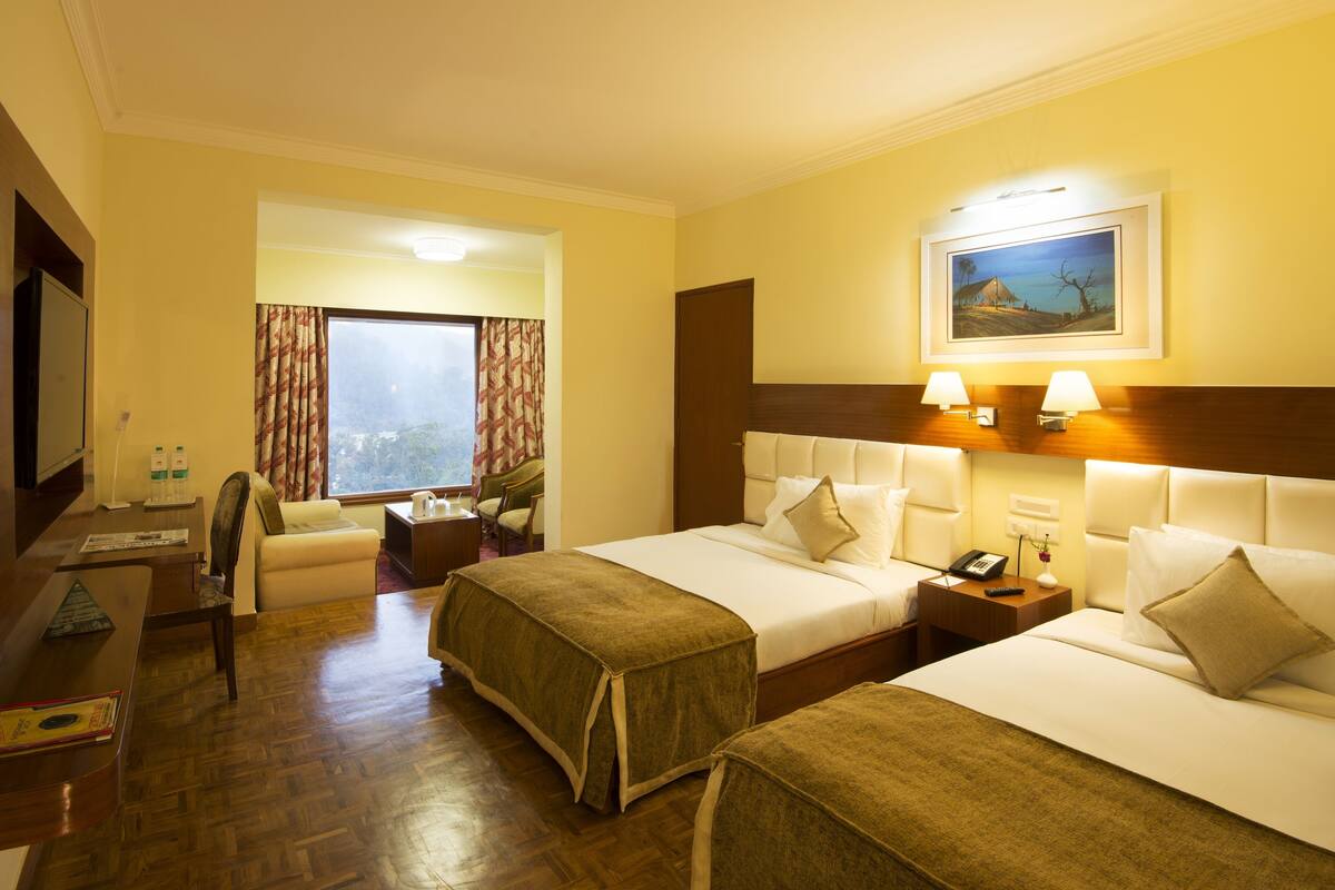 A hotel room with two beds, a desk, a chair, a TV, and a window with curtains.