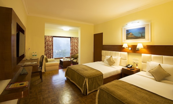 A hotel room with two beds, a desk, a chair, a TV, and a window with curtains.