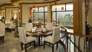 A restaurant with a terrace, large windows, and a view of the outdoors. - Gem Park Ooty (Ootacamund)