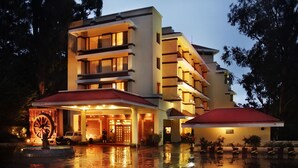 A multi-story hotel with a red-tiled roof, a water feature in front, and a well-lit entrance. - Gem Park Ooty (Ootacamund)