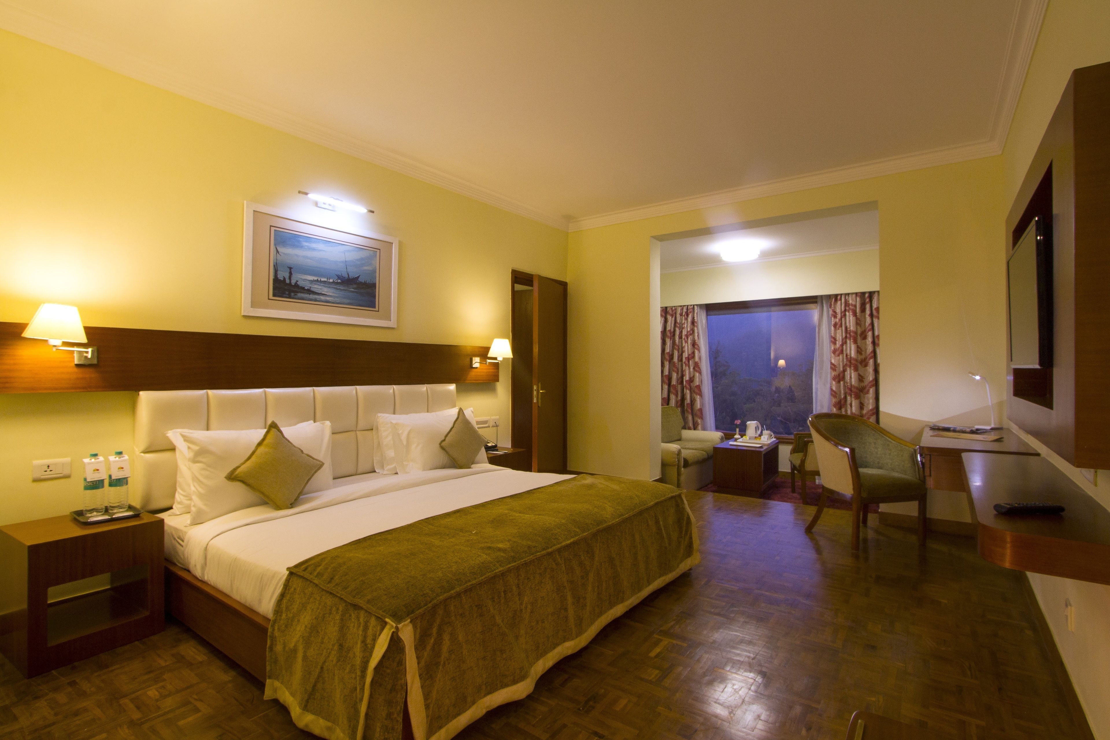Habitación de hotel con una cama grande, lámparas de noche, un escritorio con silla, un televisor y una ventana con cortinas.