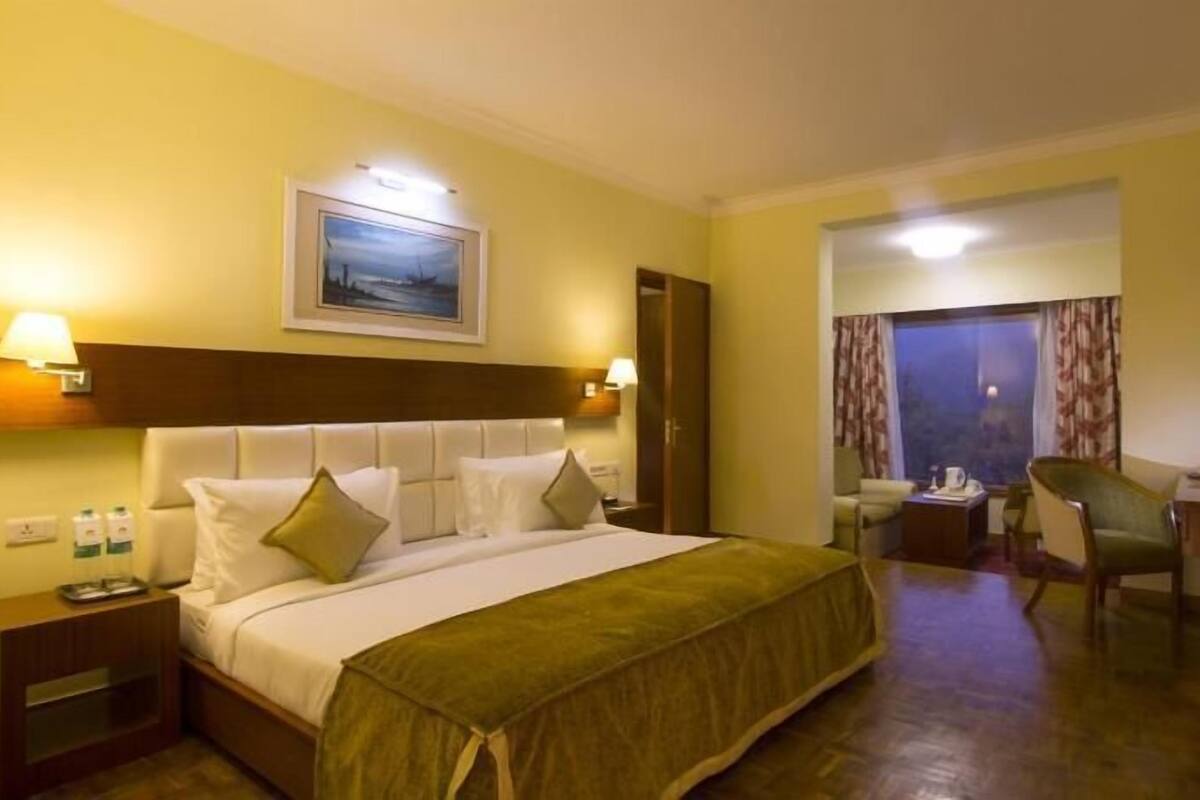 A hotel room with a bed, bedside tables, a desk, a chair, a television, and a window with curtains.