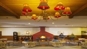A lobby with a fireplace, chandeliers, and wicker furniture. - Gem Park Ooty (Ootacamund)