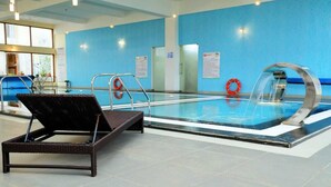 An indoor swimming pool with a lounge chair, a water feature, and safety signs. - Gem Park Ooty (Ootacamund)