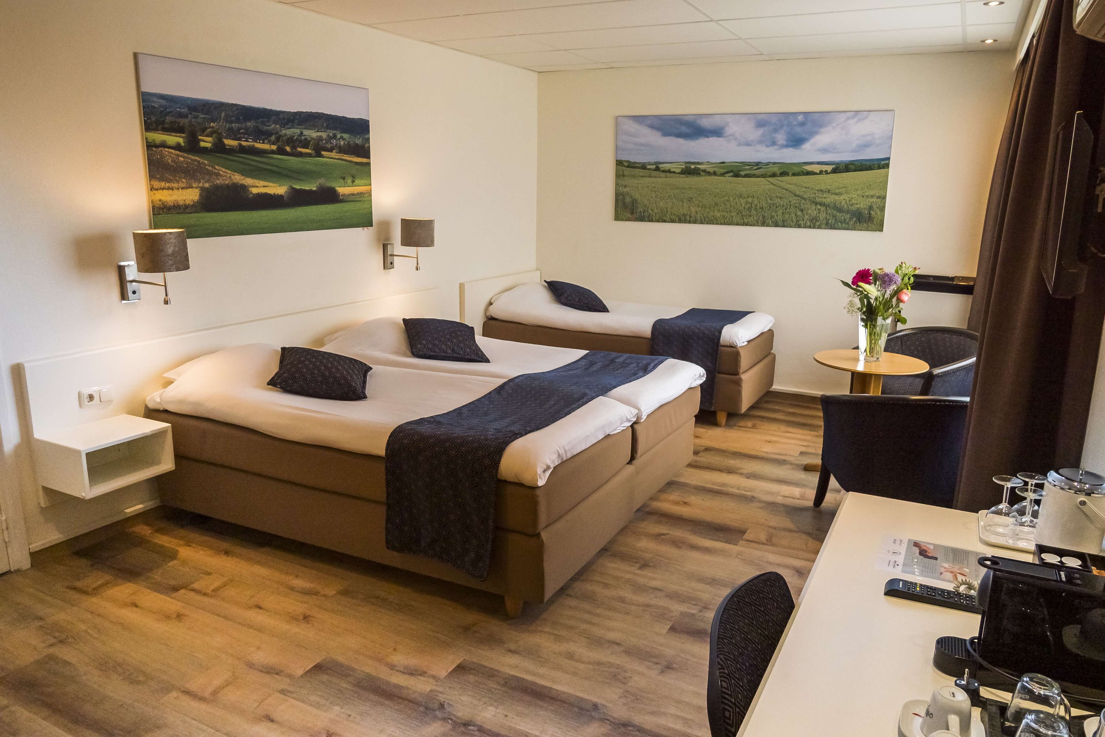 Een hotelkamer met twee bedden, een bureau met een koffiezetapparaat, en twee schilderijen aan de muur.