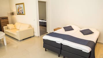 A hotel room with a bed, a sofa, a desk, and a painting on the wall.