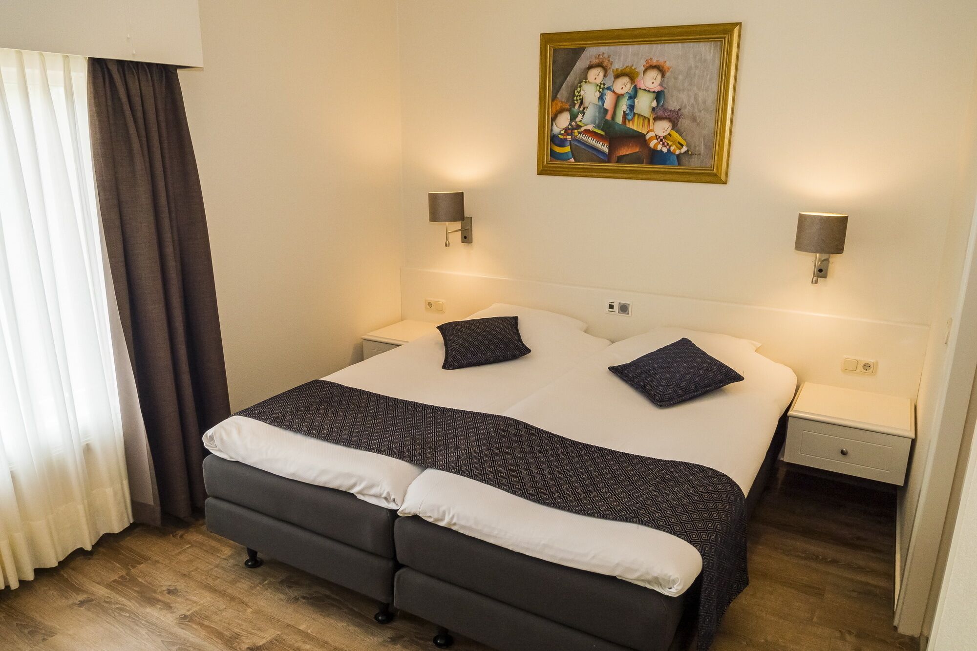 A hotel room with a bed, two bedside tables, a nightstand, a painting on the wall, and a window with curtains.