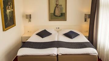 A double bed with two pillows, a painting on the wall, and a nightstand with a lamp.