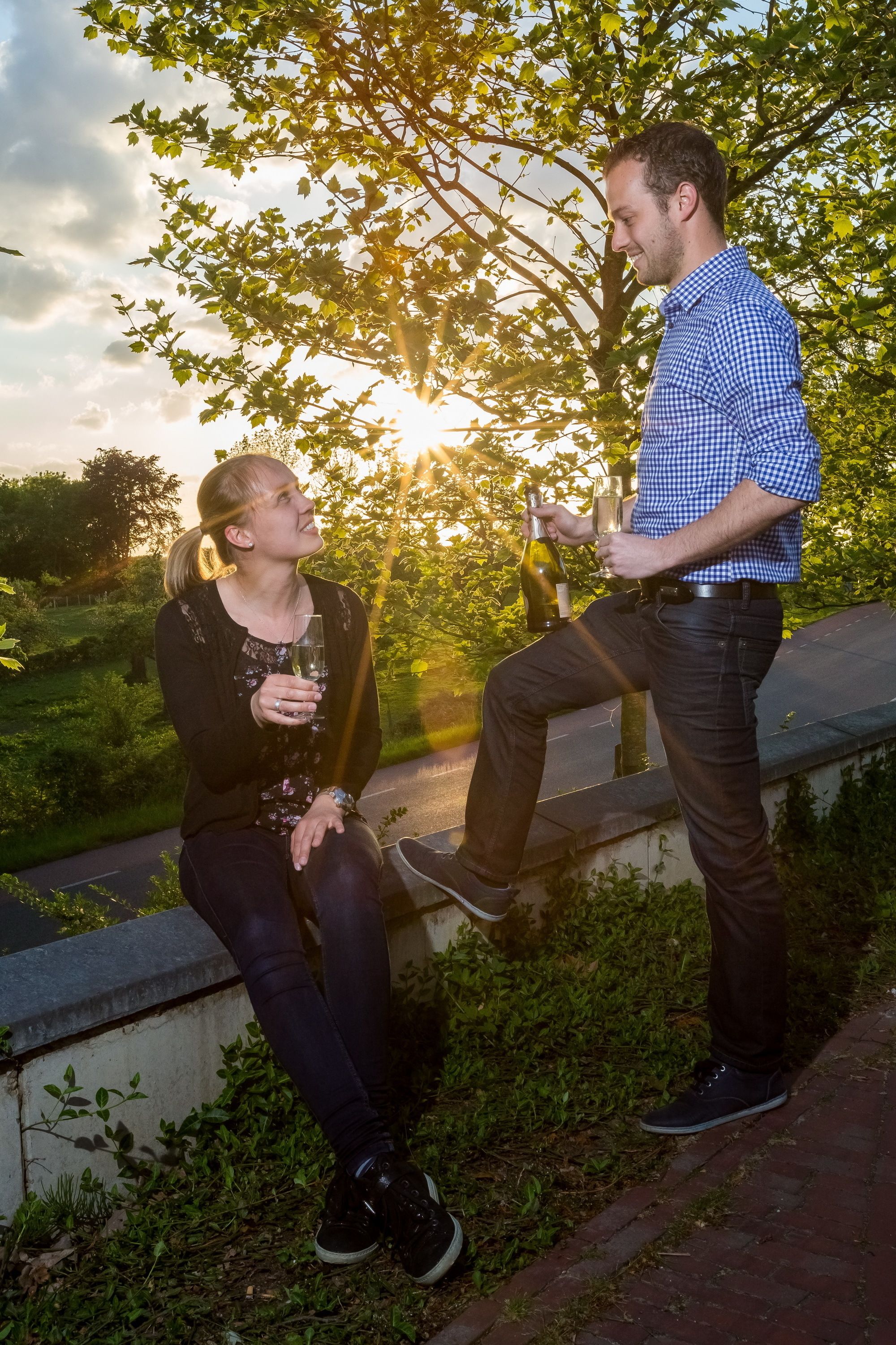 Two people sitting on a ledge outdoors with a sunset in the background.