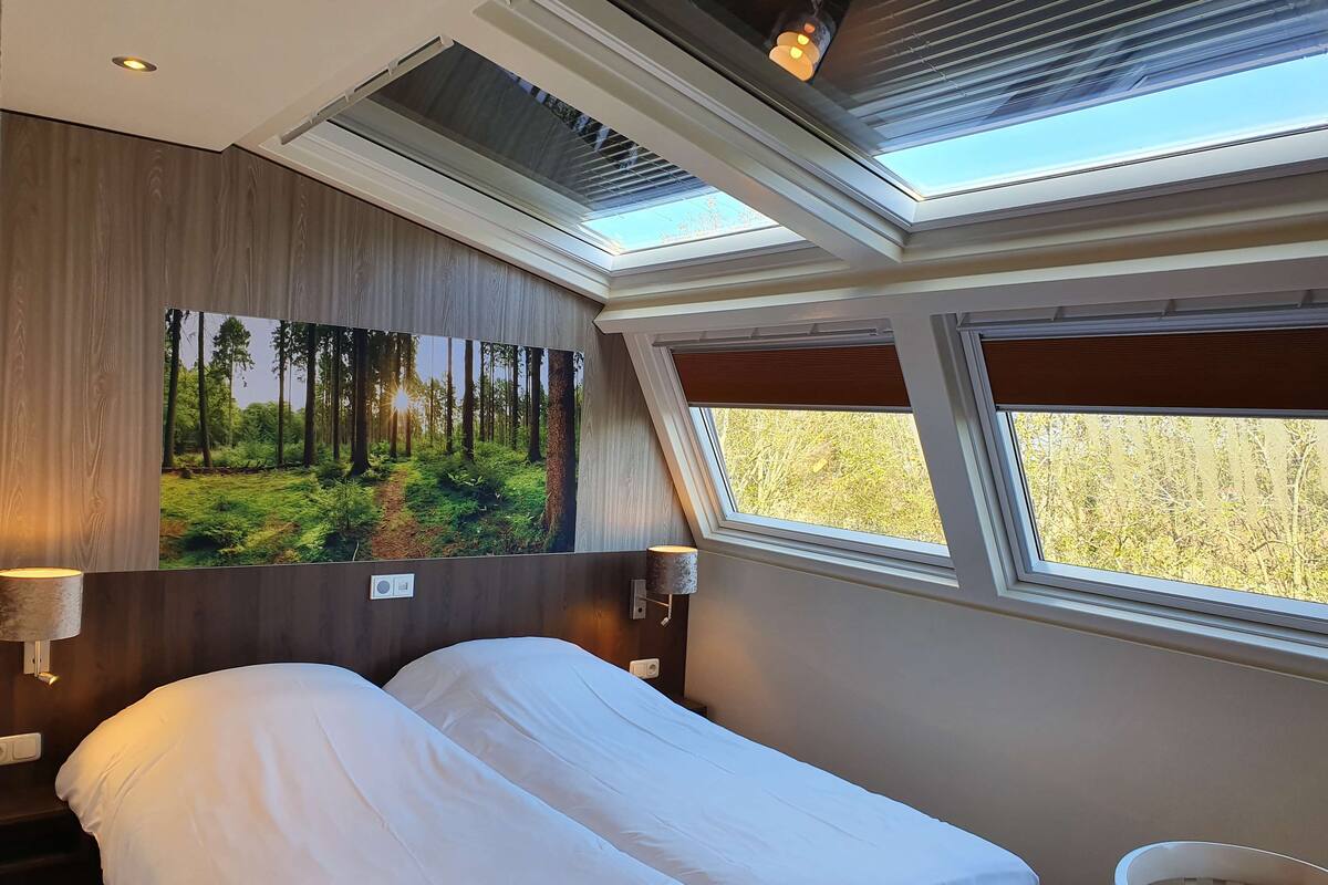 Une chambre dotée d’un grand lit, de fenêtres de toit, d’une fresque murale sur le thème de la forêt et offrant une vue sur l’extérieur.