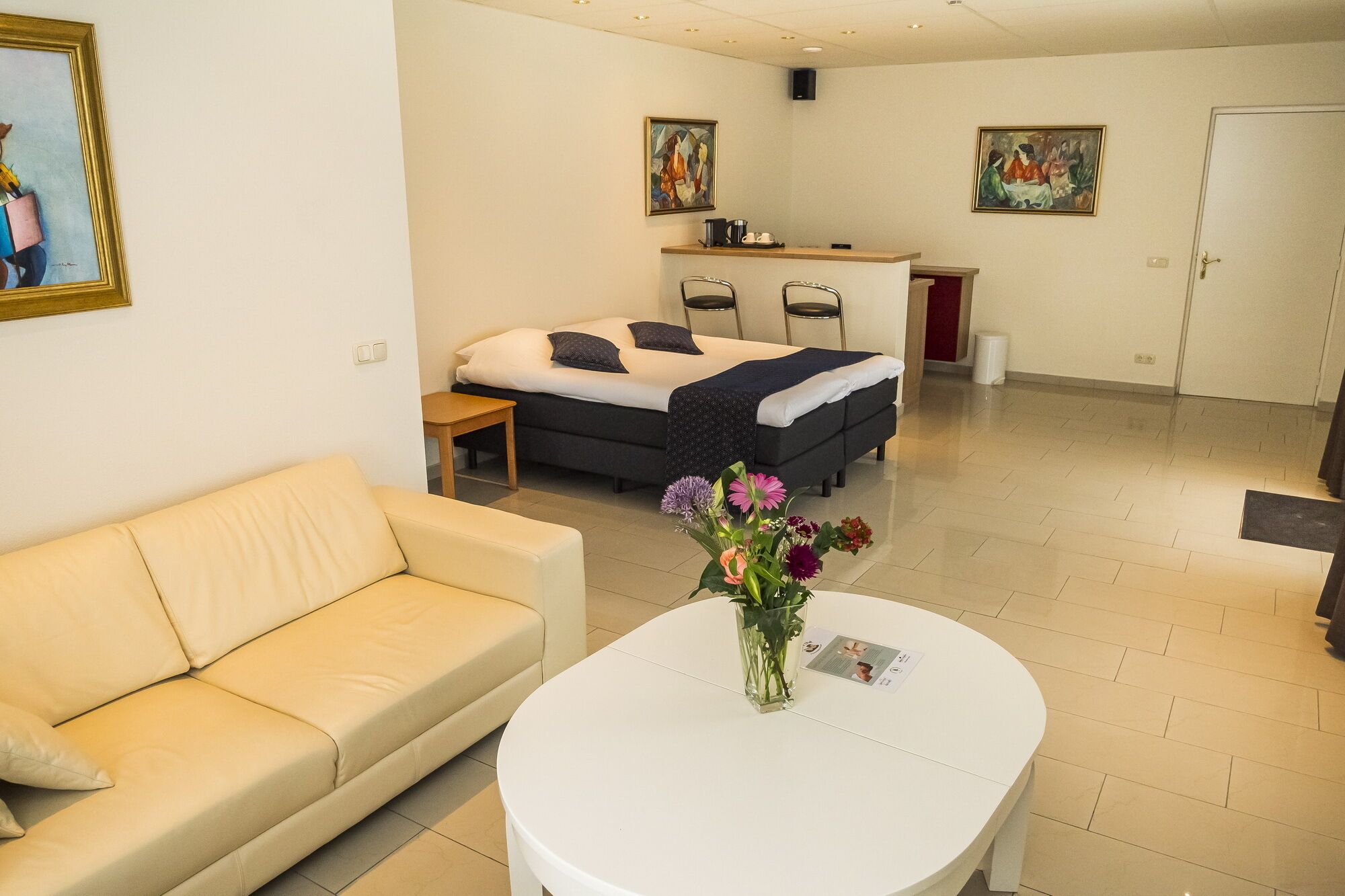 Una habitación de hotel moderna con una cama, un sofá, una mesita con un florero y dos cuadros en las paredes.