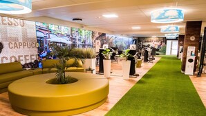 Een moderne receptie met een groen vloerkleed, een grote bank en een muur met een digitale scherm waarop een stadsgezicht te zien is.