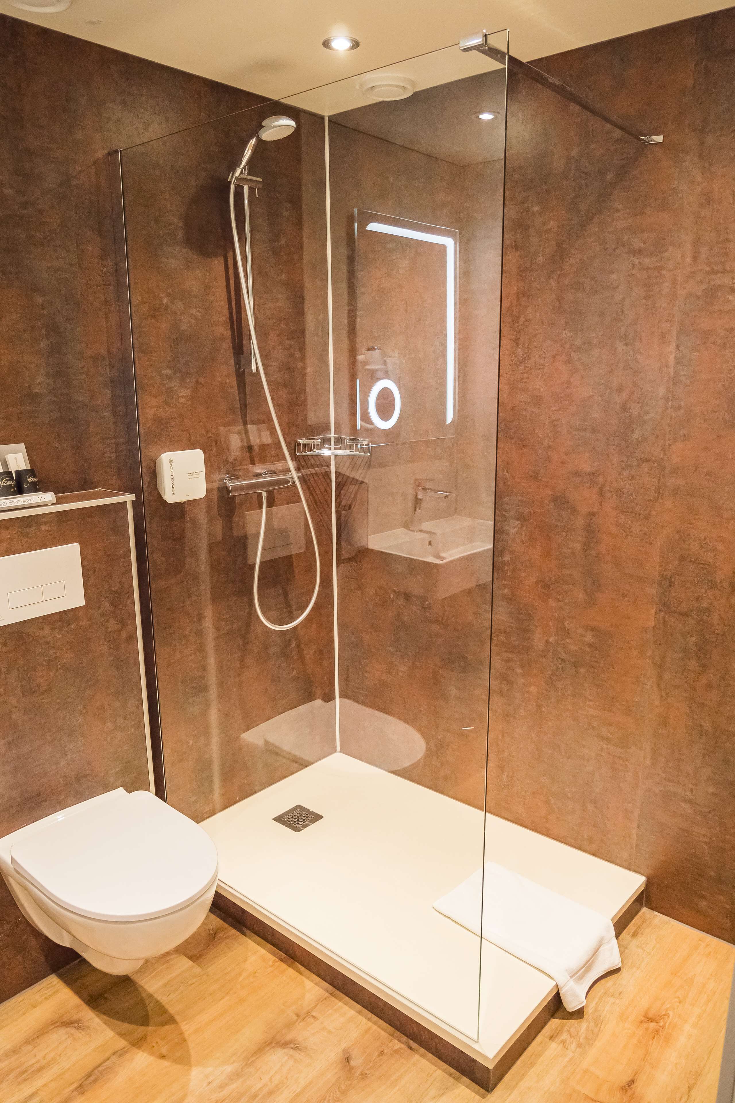 Ein modernes Badezimmer mit einer gläsernen Duschkabine, einer weißen Toilette und einem Holzbadezimmer-Möbel.
