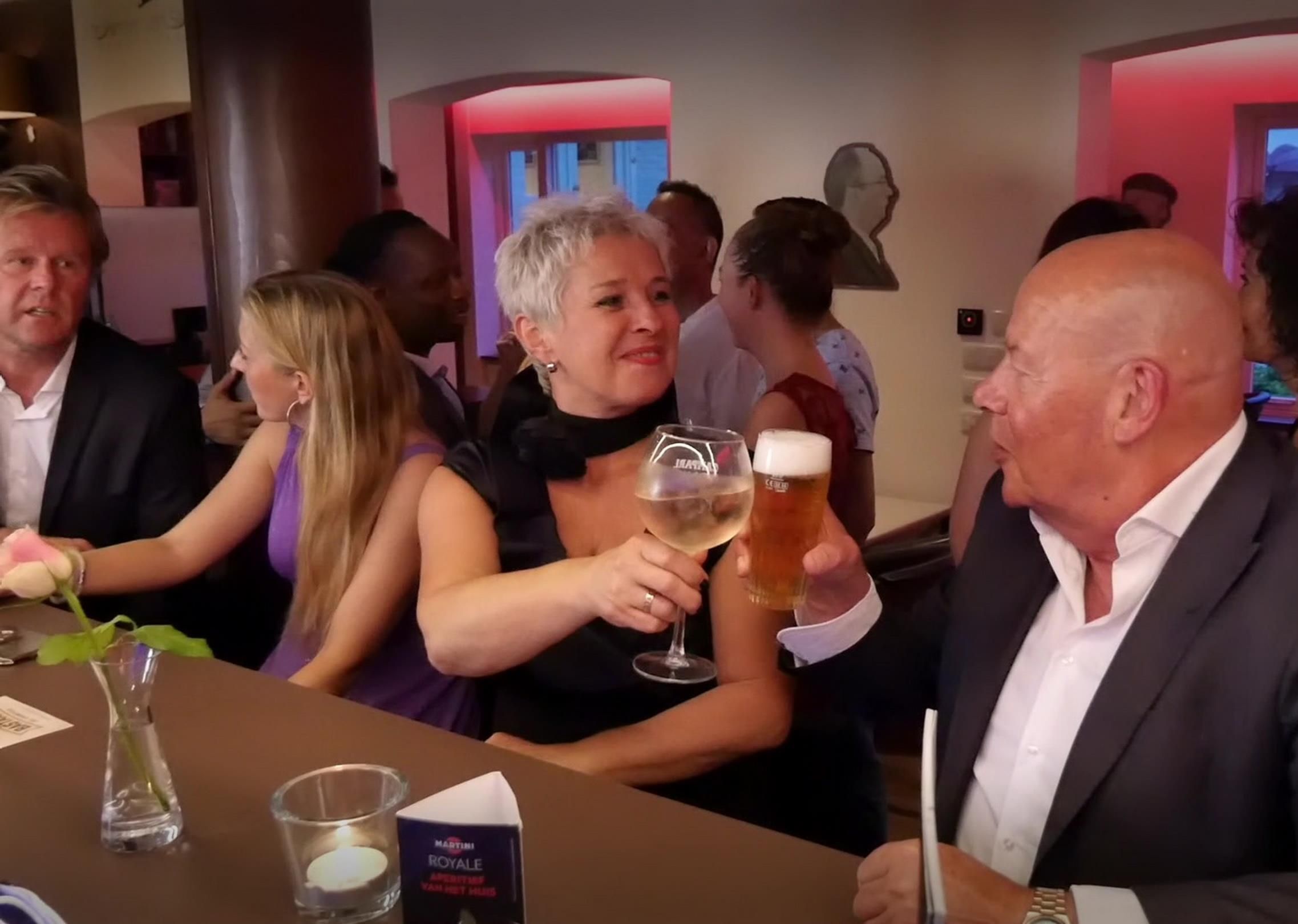 Eine Gruppe von Personen sitzt an einem Tisch in einem Restaurant, eine Kerze und eine Speisekarte sind sichtbar.