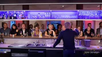 A bar area with a long counter, multiple shelves with bottles and glasses, and a sink.