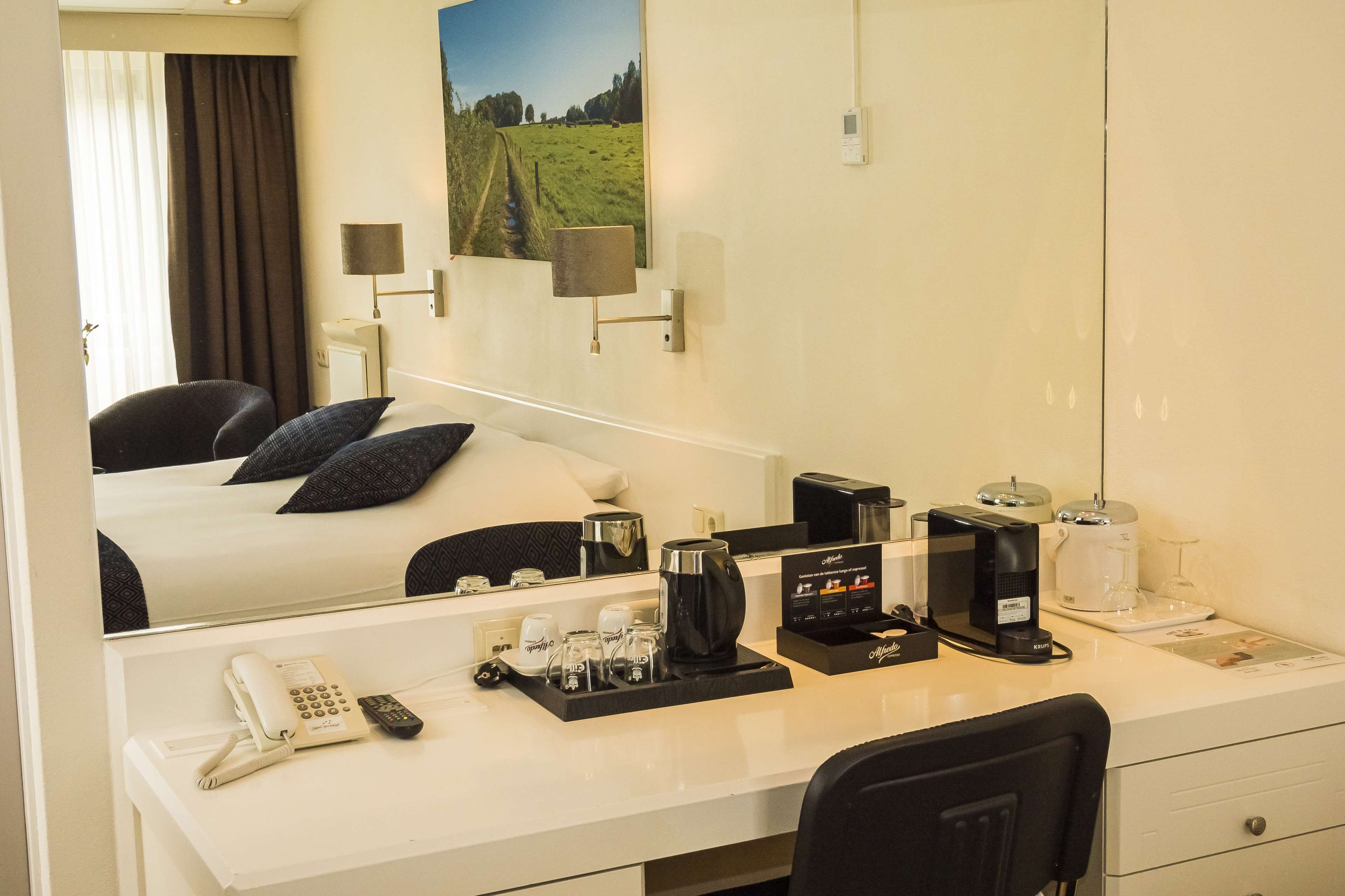 A hotel room with a bed, a desk with a telephone, coffee maker, and a coffee pot.
