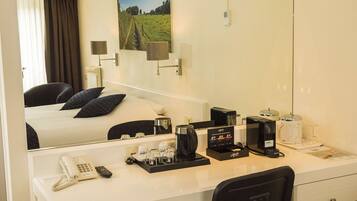A hotel room with a bed, a desk with a telephone, coffee maker, and a coffee pot.