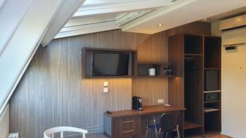 Una habitación moderna con tragaluz, televisión de pantalla plana, cafetera, escritorio y una silla.