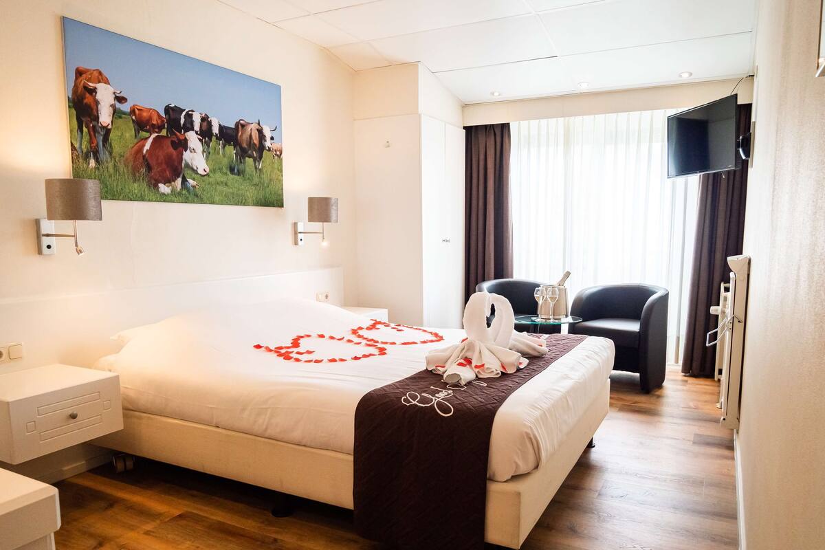 Une chambre d’hôtel avec un lit, un tableau représentant des vaches, une télévision, une chaise et un bureau.
