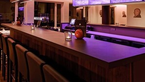 Een moderne bar met een lange toonbank, barstoelen en een plafond met neonverlichting.