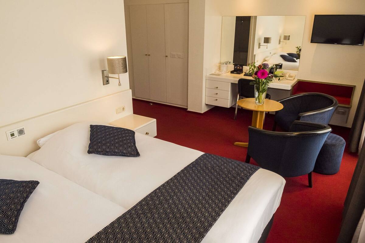 Une chambre d’hôtel avec deux lits, un bureau, une chaise, une télévision et un miroir.