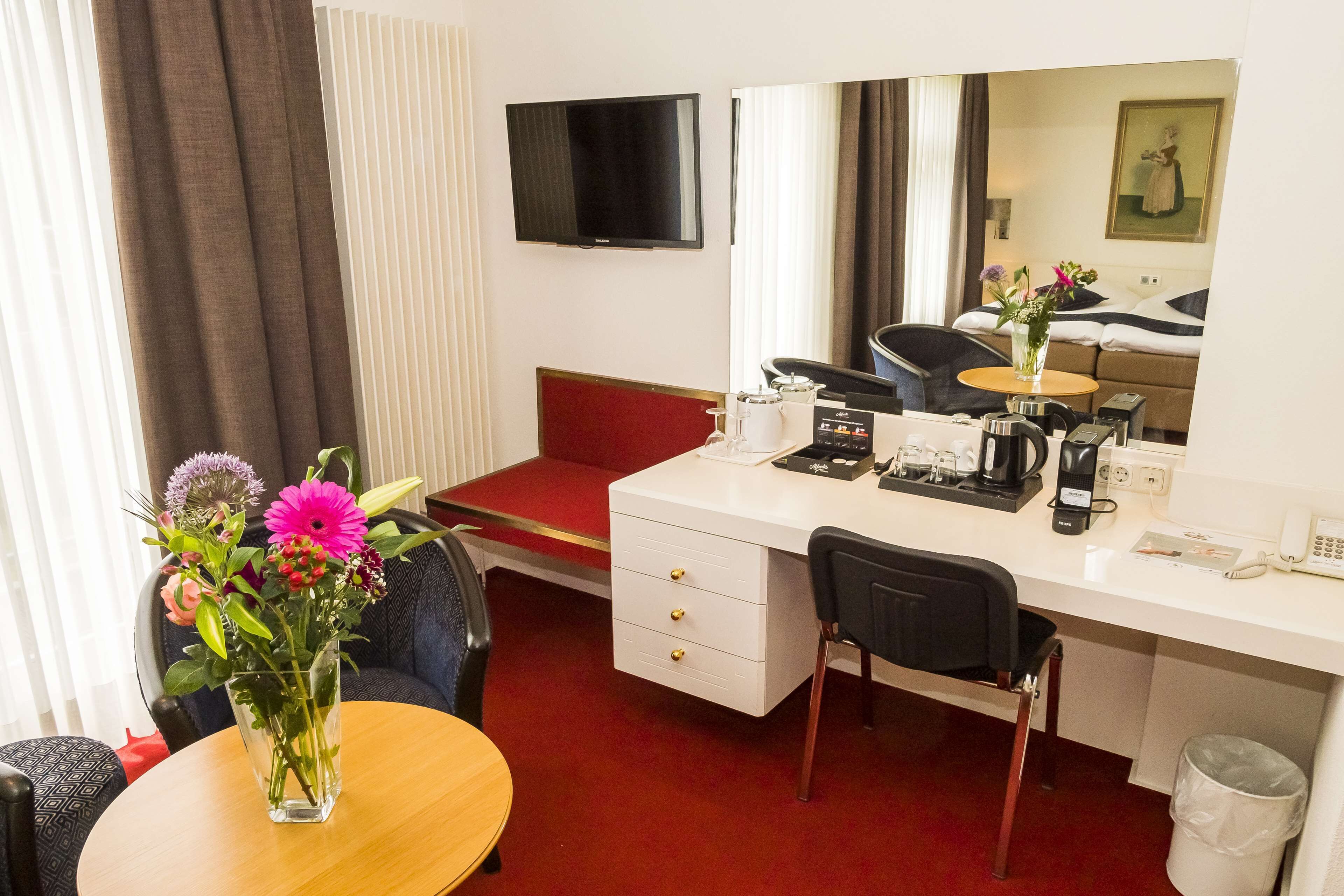 Habitación de hotel con escritorio, silla y una mesita con un jarrón de flores.