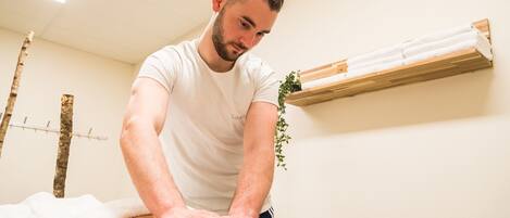 A massage therapy session in a room with a wooden shelf and a plant.
