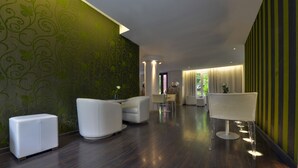 A modern hotel lobby with dark wooden flooring, white sofas, a reception desk, and a green patterned wall. - Hôtel Le Quartier Bercy Square (Paris)