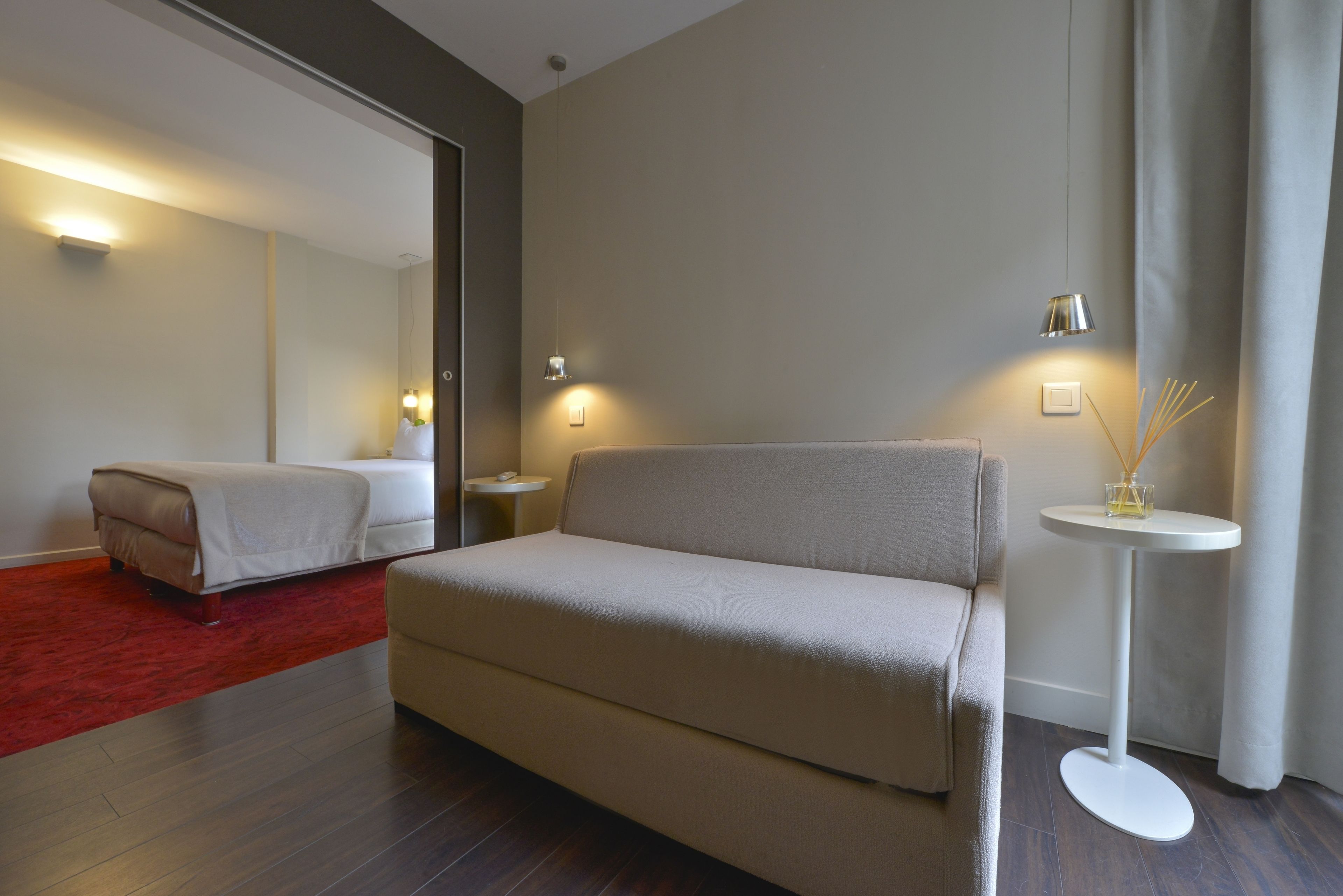 Une chambre d’hôtel avec un grand lit, un petit canapé, une table d’appoint ronde avec une lampe et un miroir au mur.